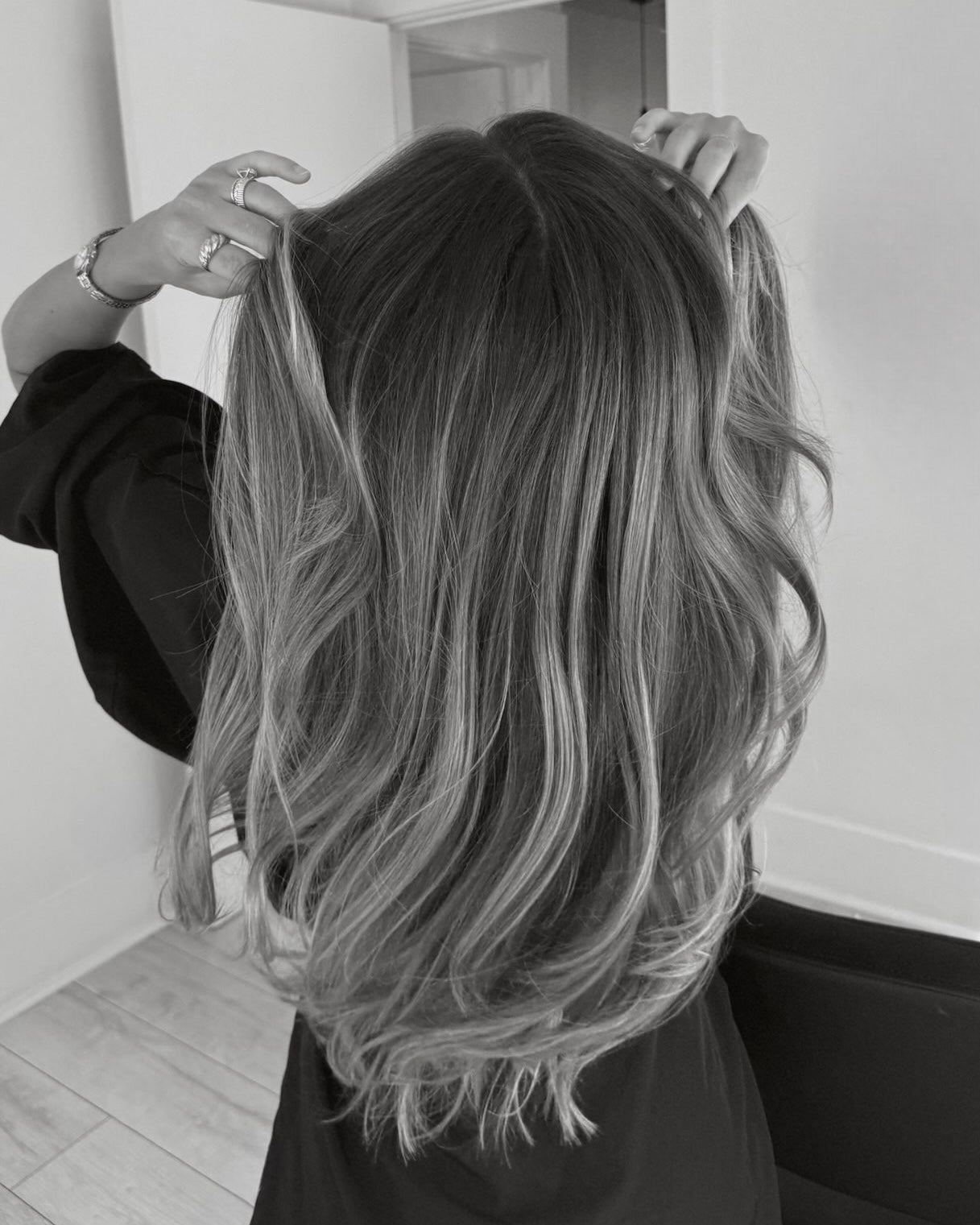 Black and white shot of a woman with long, wavy, highlighted hair, hands touching her head.