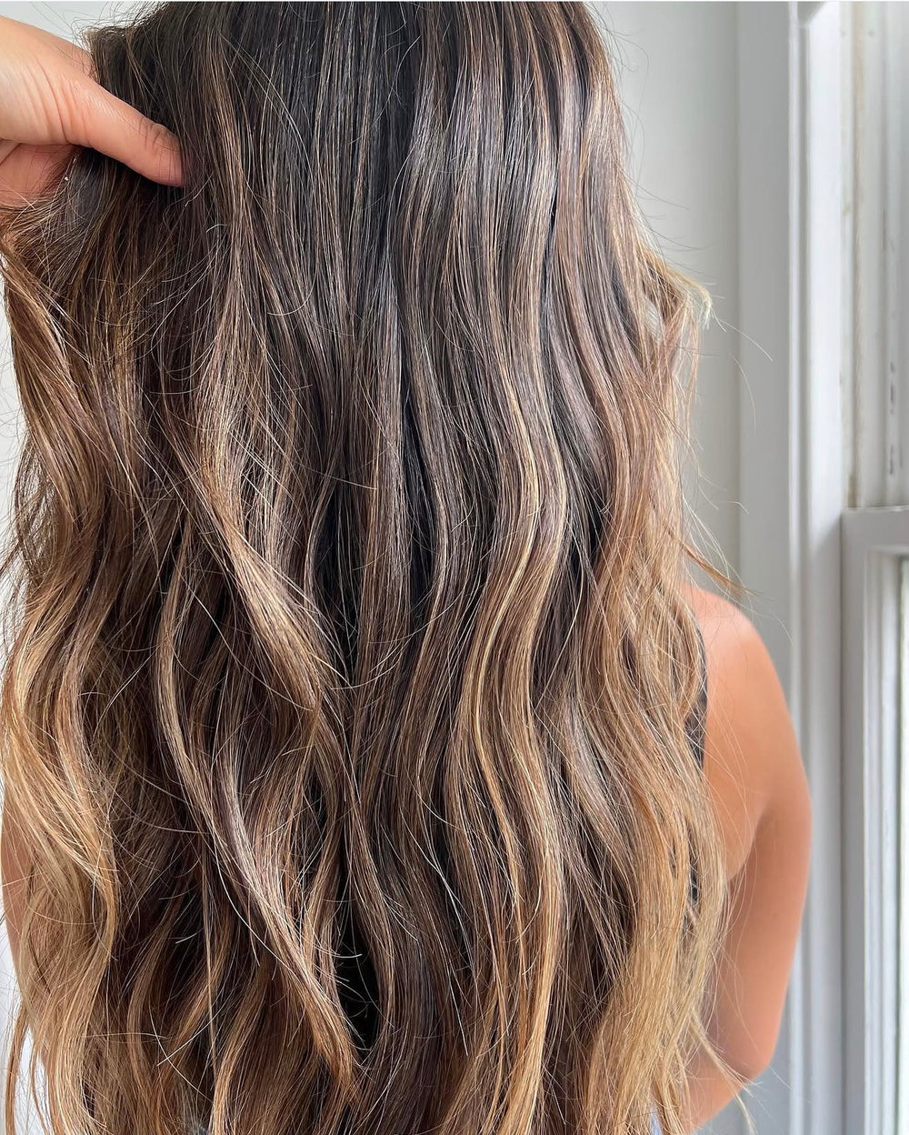 Long, wavy brown hair with golden blonde balayage highlights, styled from behind.