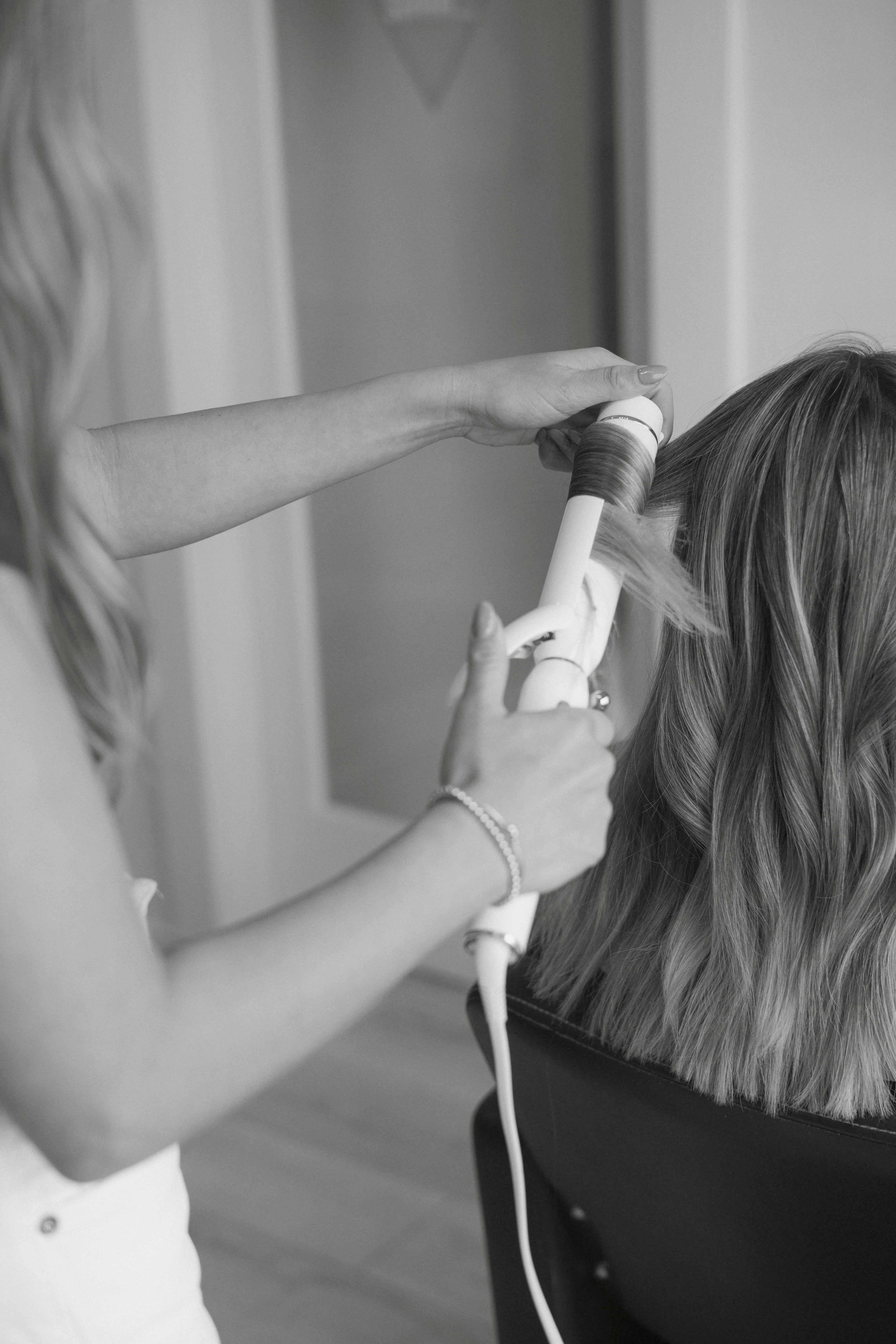 Stylist curling long, wavy hair with a white curling iron; black and white photo.