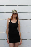 Woman in black ribbed fitted tank mini dress, size S, with a camo cap.