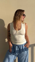 Woman in a white ribbed U-neck cotton Coco Tank top and blue pants, wearing sunglasses.