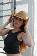Woman with red hair wearing a light brown woven straw cowgirl hat and black tank top.