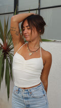 Woman in a white ruched cotton spandex halter top, light wash denim shorts, and charm necklace.
