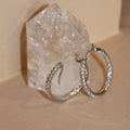 Sparkling silver hoop earrings with clear cubic zirconia stones, displayed on a quartz crystal.