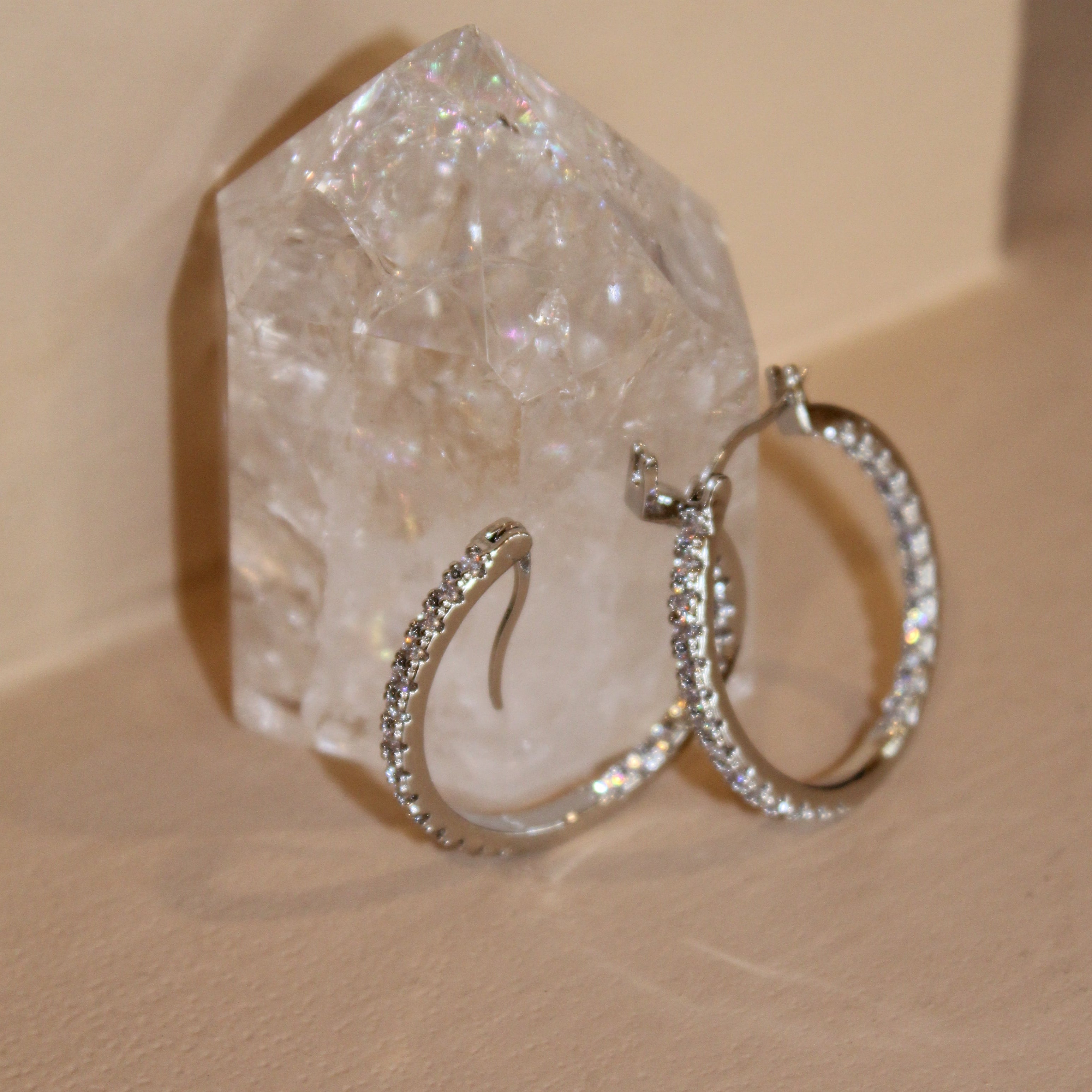 Sparkling silver hoop earrings with clear cubic zirconia stones, displayed on a quartz crystal.