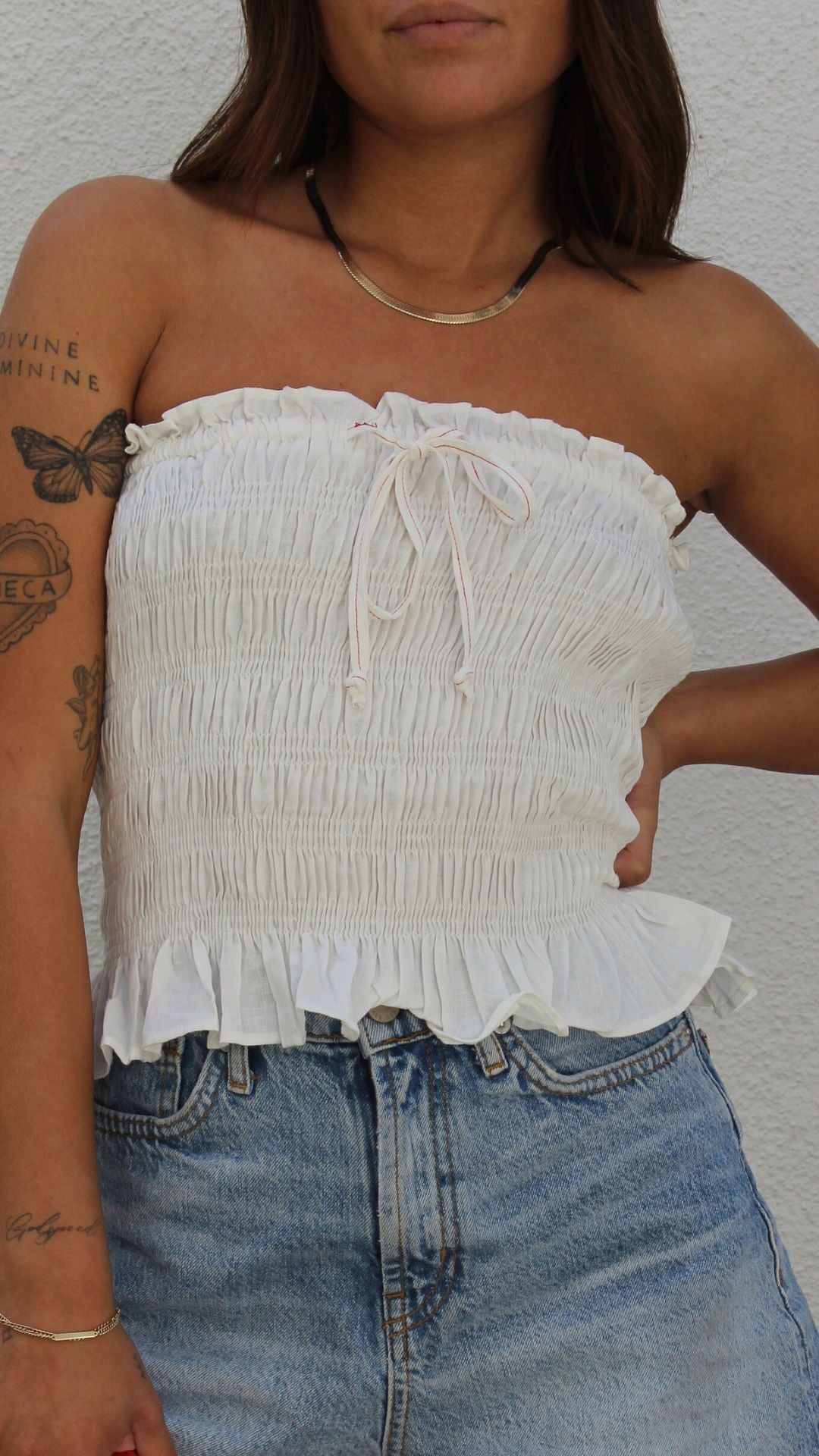 White smocked tube top in viscose-linen blend with ruffled hem and front tie detail.