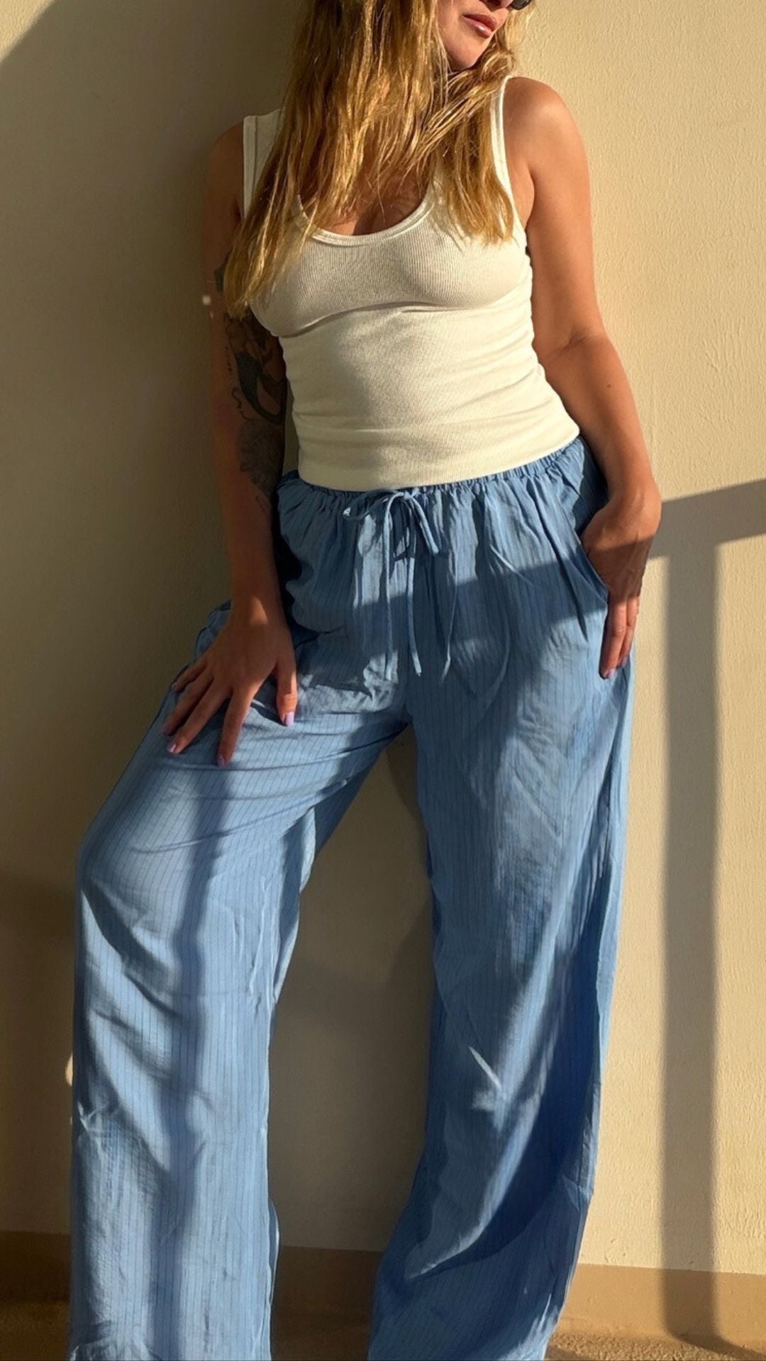 Woman in a white tank top and light blue Hang Loose baggy pants with vertical stripes and a drawstring waist.