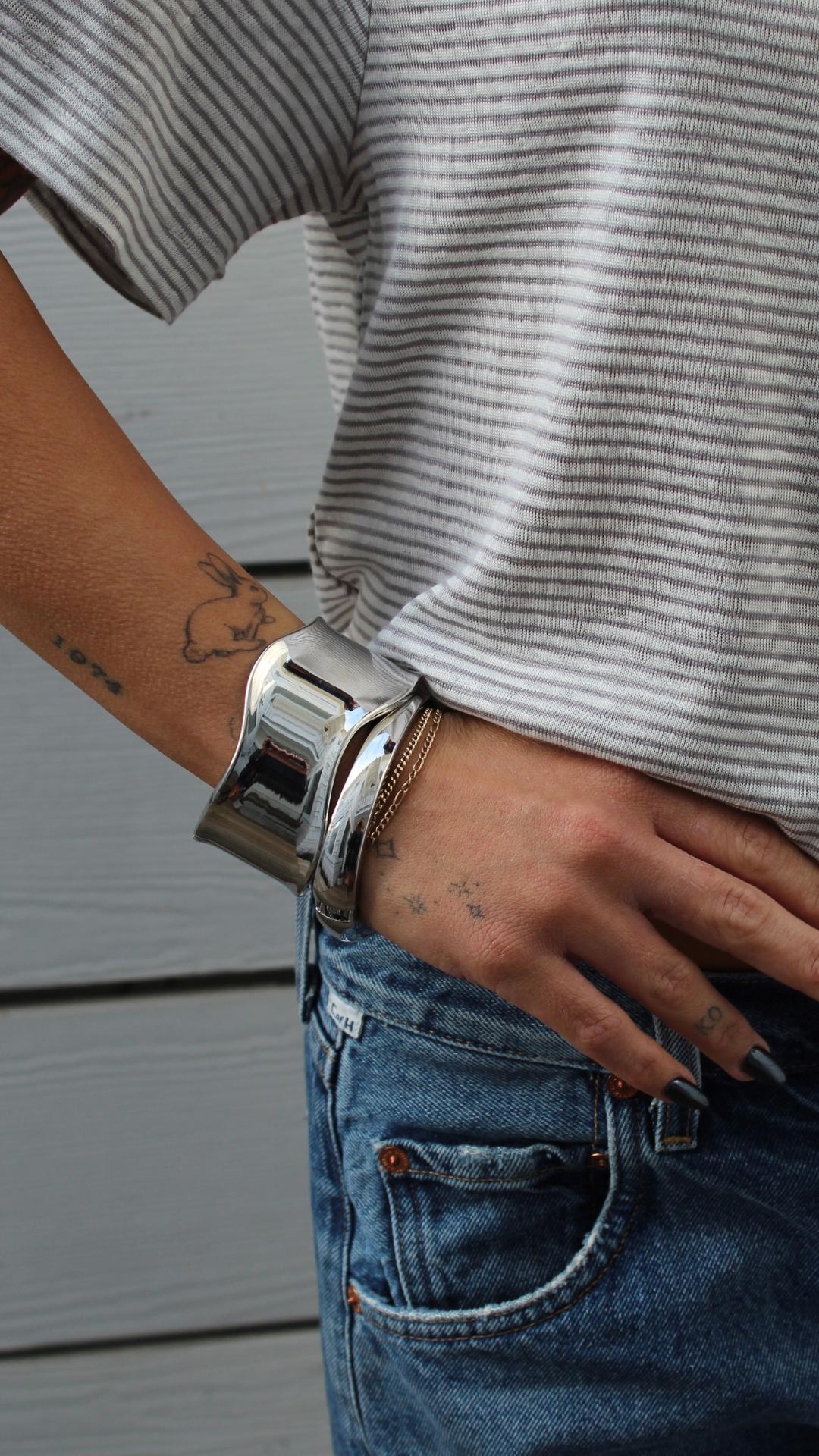 High Tide Cuff: Thick, wavy silver bracelet on a wrist with a striped shirt and jeans.
