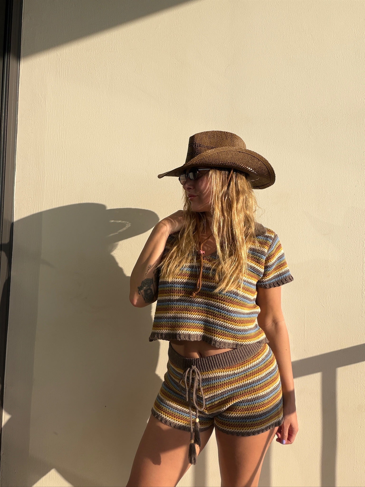 Woman in a brown crochet knit striped top and matching shorts with a cowboy hat.