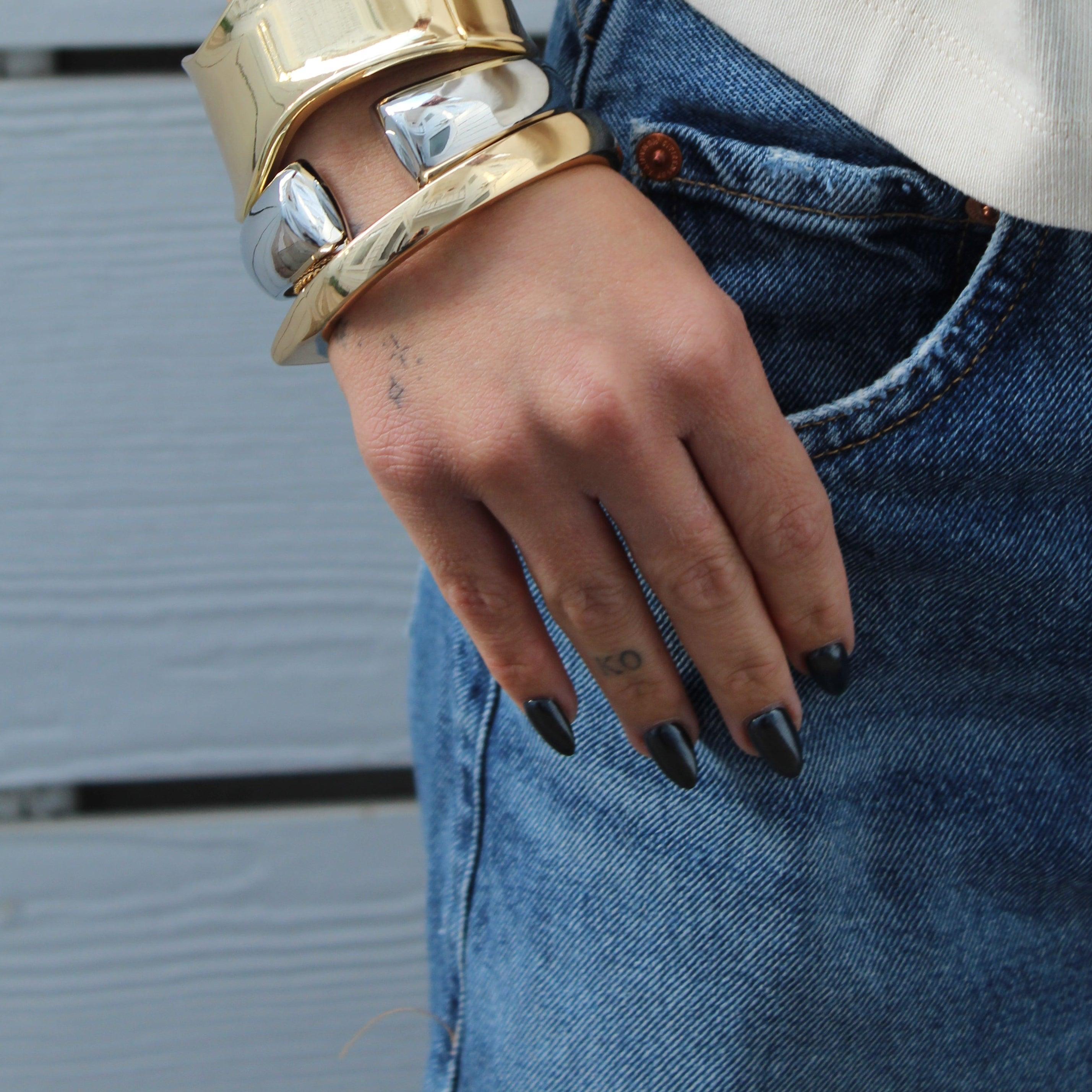 Gold and silver mini cuffs stacked on a wrist, with a hand in a jeans pocket.