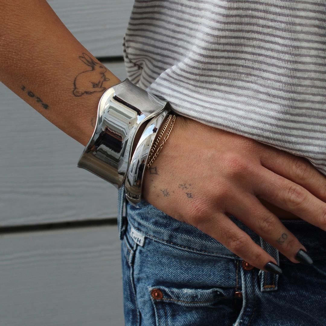 Silver Mini High Tide Cuff bracelet on a tattooed arm, worn with jeans and a striped shirt.