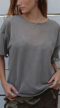 Woman in a sheer metallic silver boxy top with under tank, short sleeves, and a heart necklace.
