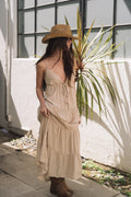 Model in a beige tiered maxi prairie dress with spaghetti straps and a straw hat.