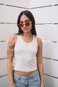 Woman in a ribbed fitted basic light grey tank top, light wash jeans, and orange sunglasses.
