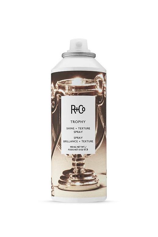 R+Co Trophy Shine + Texture Spray, 6oz white aerosol can with a shiny gold trophy graphic and black label.