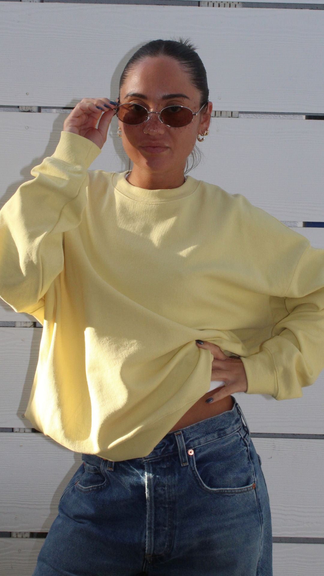 Model in a light yellow oversized crewneck sweatshirt, size S, with blue jeans and sunglasses.