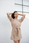 Woman in a tan waffle-knit Salty Mane bath robe with a tied belt, hands in hair.