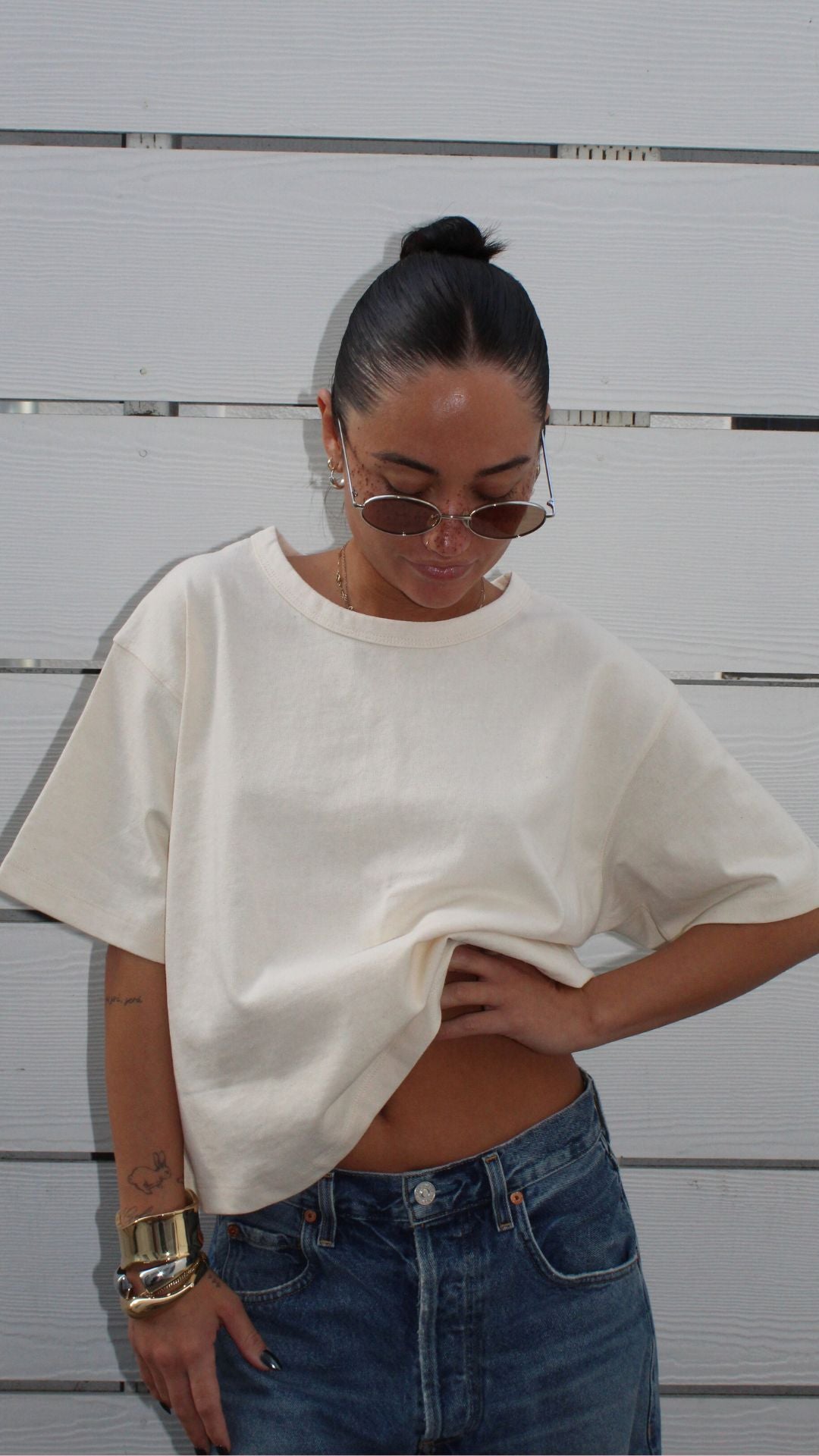 Model in a relaxed fit, off-white 100% cotton Sandy Tee, paired with jeans and sunglasses.