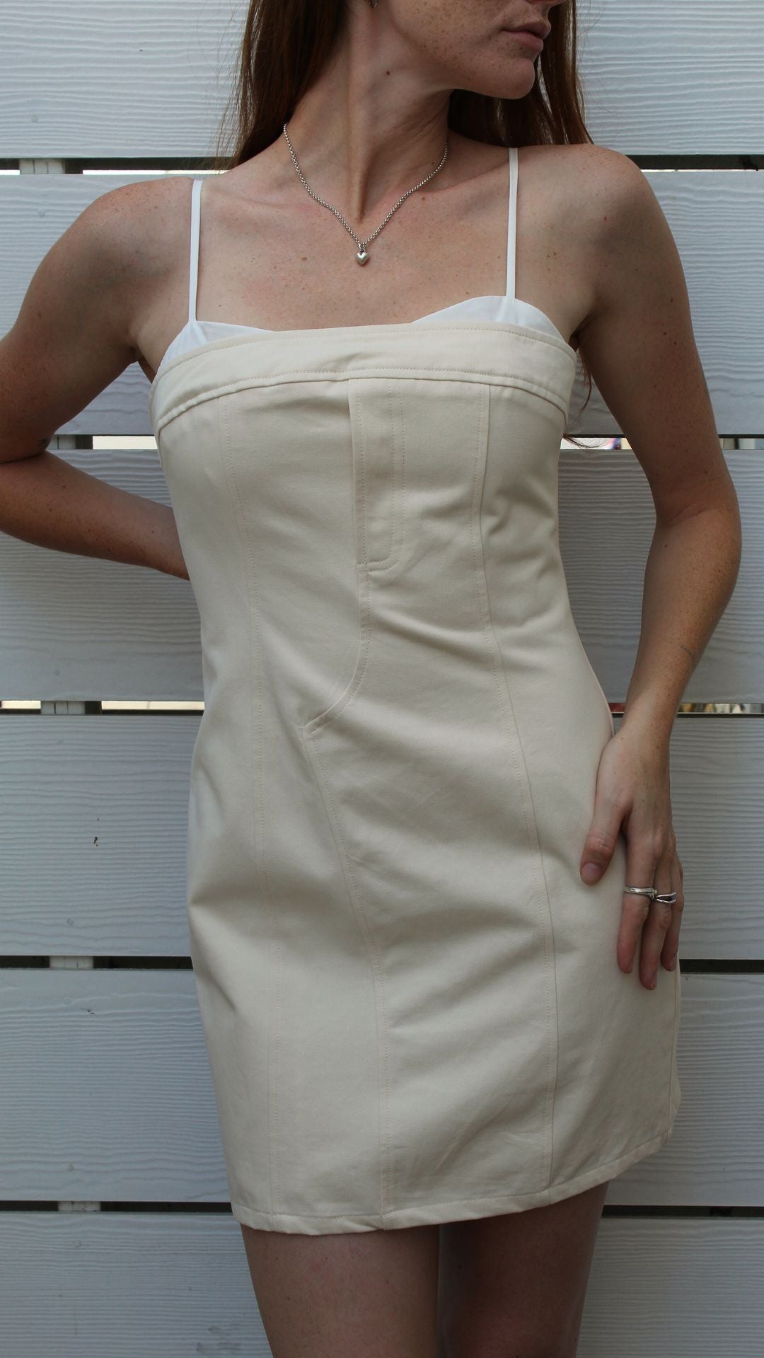 Woman in a cream cotton tank mini dress with white straps and a silver seashell necklace.