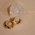 Pair of shiny gold chunky hoop earrings in front of a clear crystal.