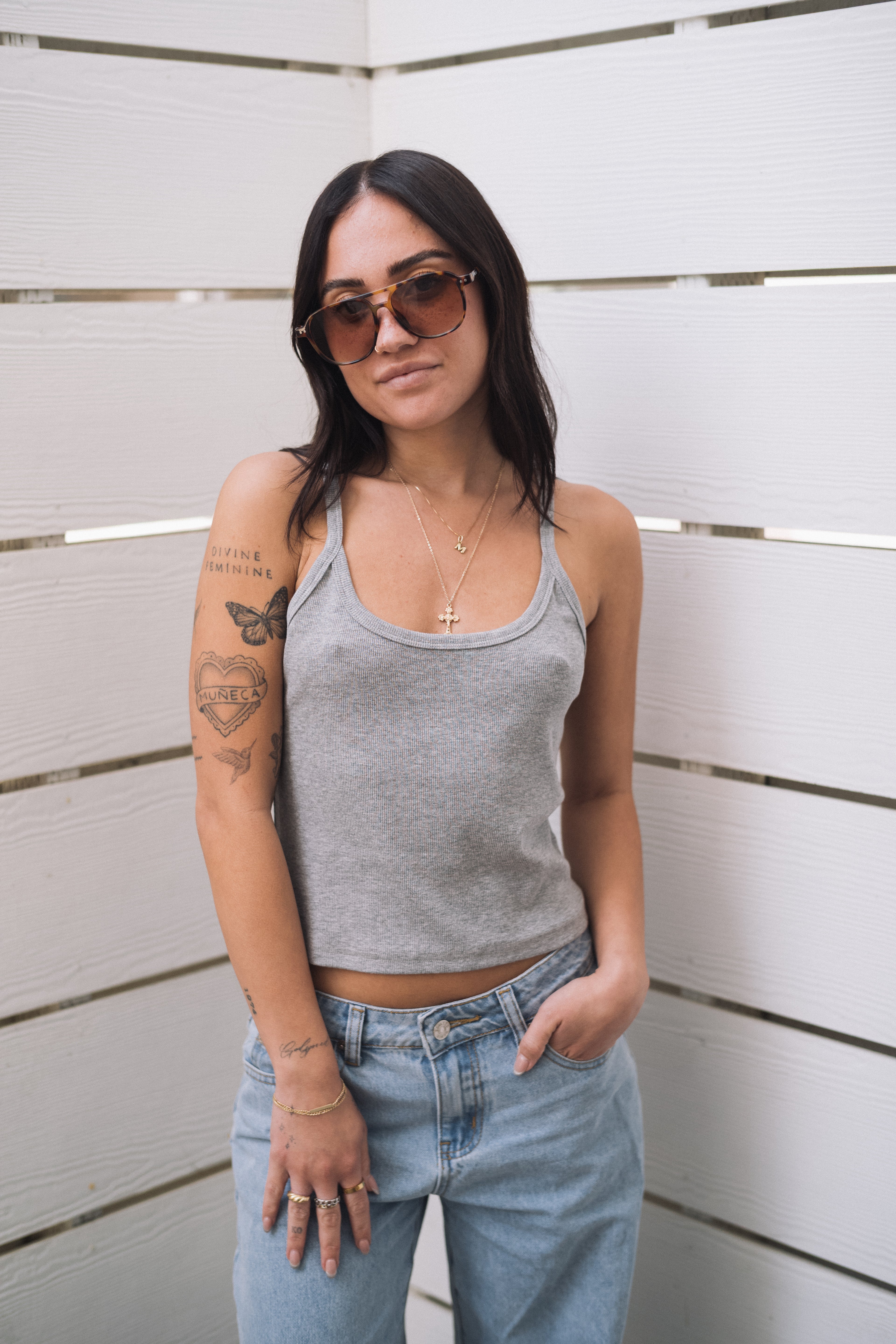 Woman in a grey ribbed scoop neck tank top, light wash jeans, and sunglasses.